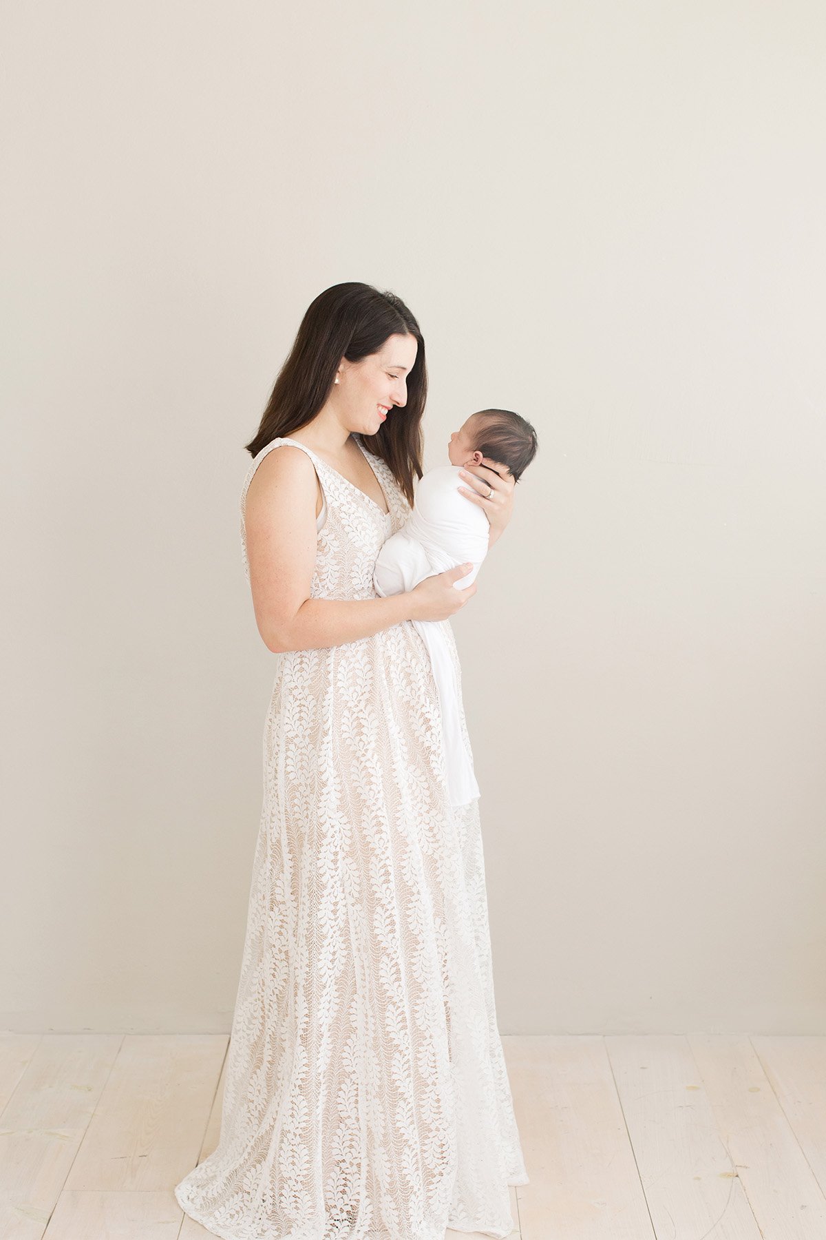 Mom wears white lace dress while holding newborn baby at Louisville Ky photography studio