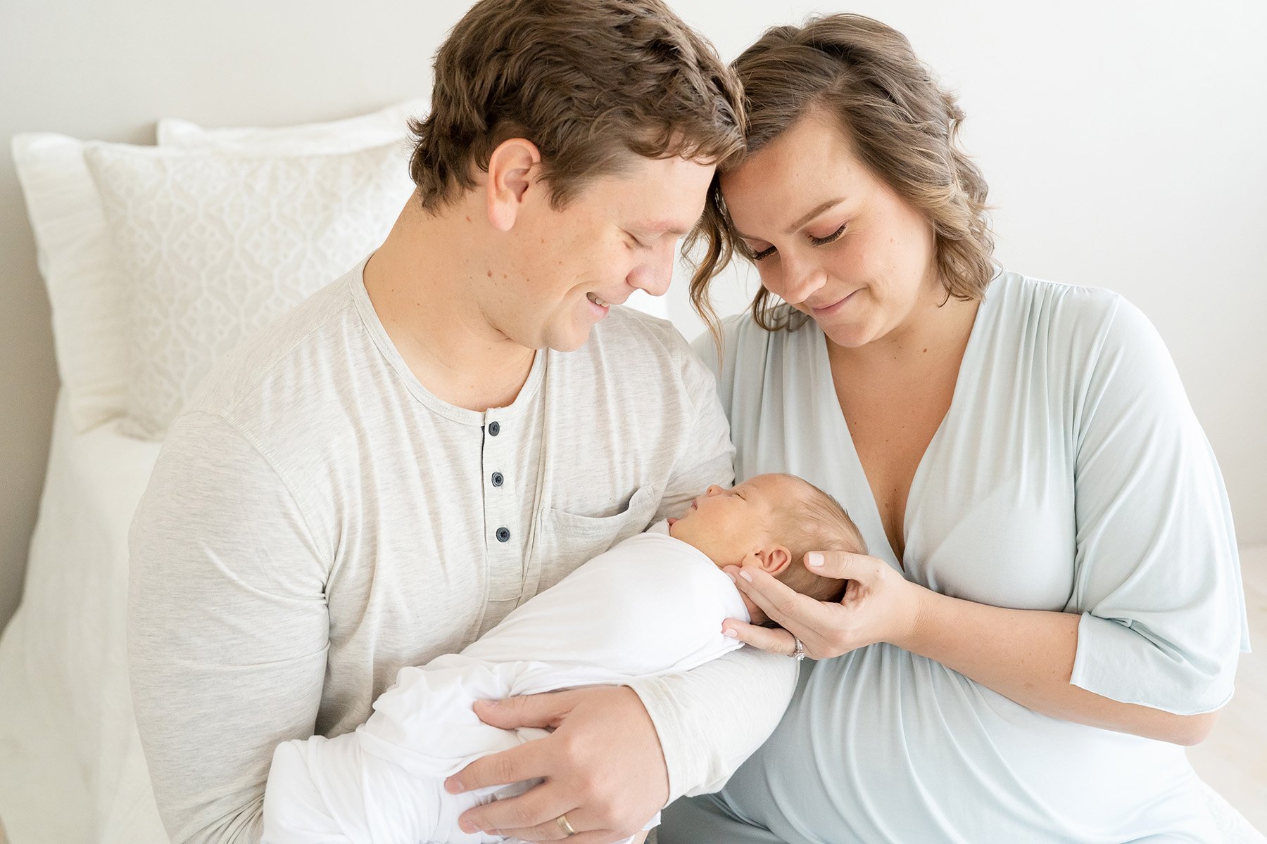 Dad and mom hold sleeping newborn baby. Mom is wearing clothing from Julie Brock Photography for the newborn session.