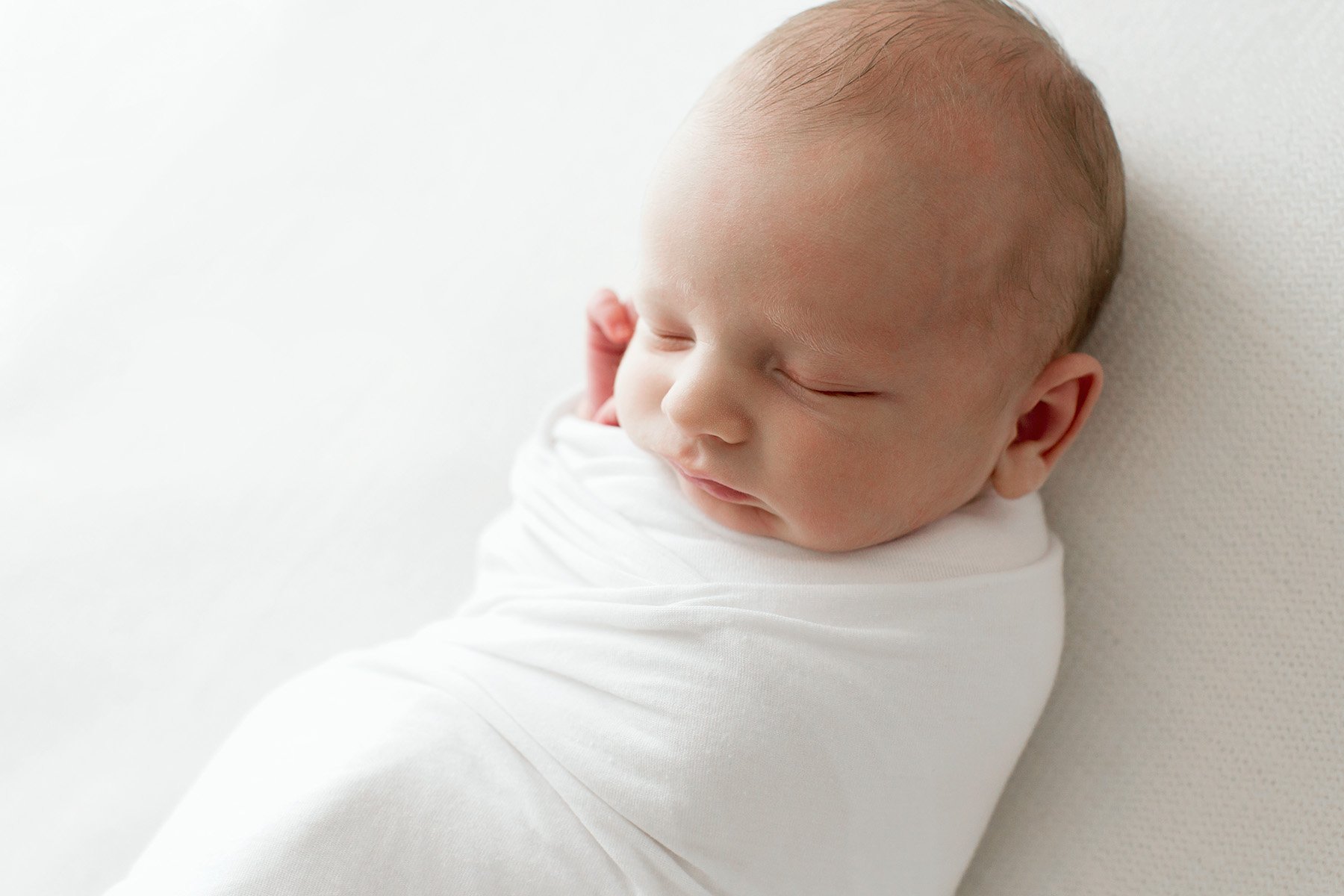 Sleeping baby boy wrapped in a white swaddle is photographed by Julie Brock Photography in Louisville KY
