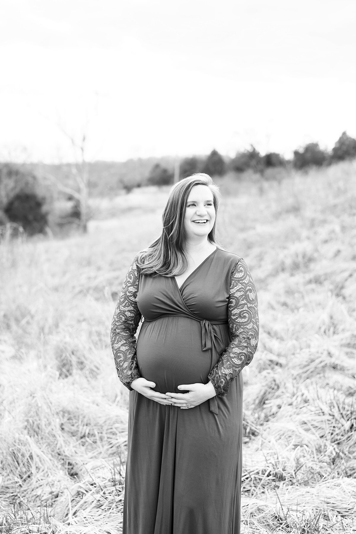 Smiling expectant mother holds her baby bump at stunning outdoor location for photos in Louisville KY.