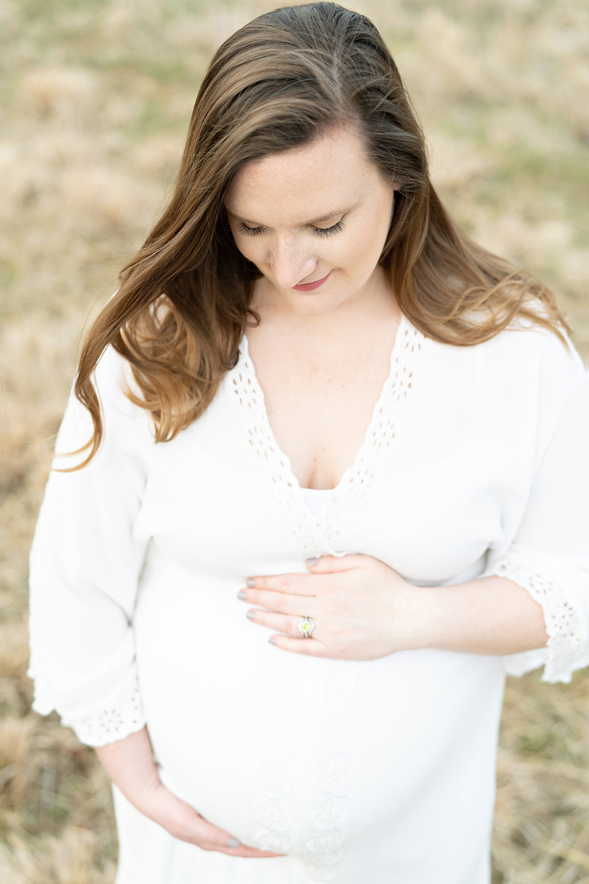 Mom looks down and holds her pregnant belly during outdoor maternity photo session with Julie Brock Photography in Louisville KY in the Parklands