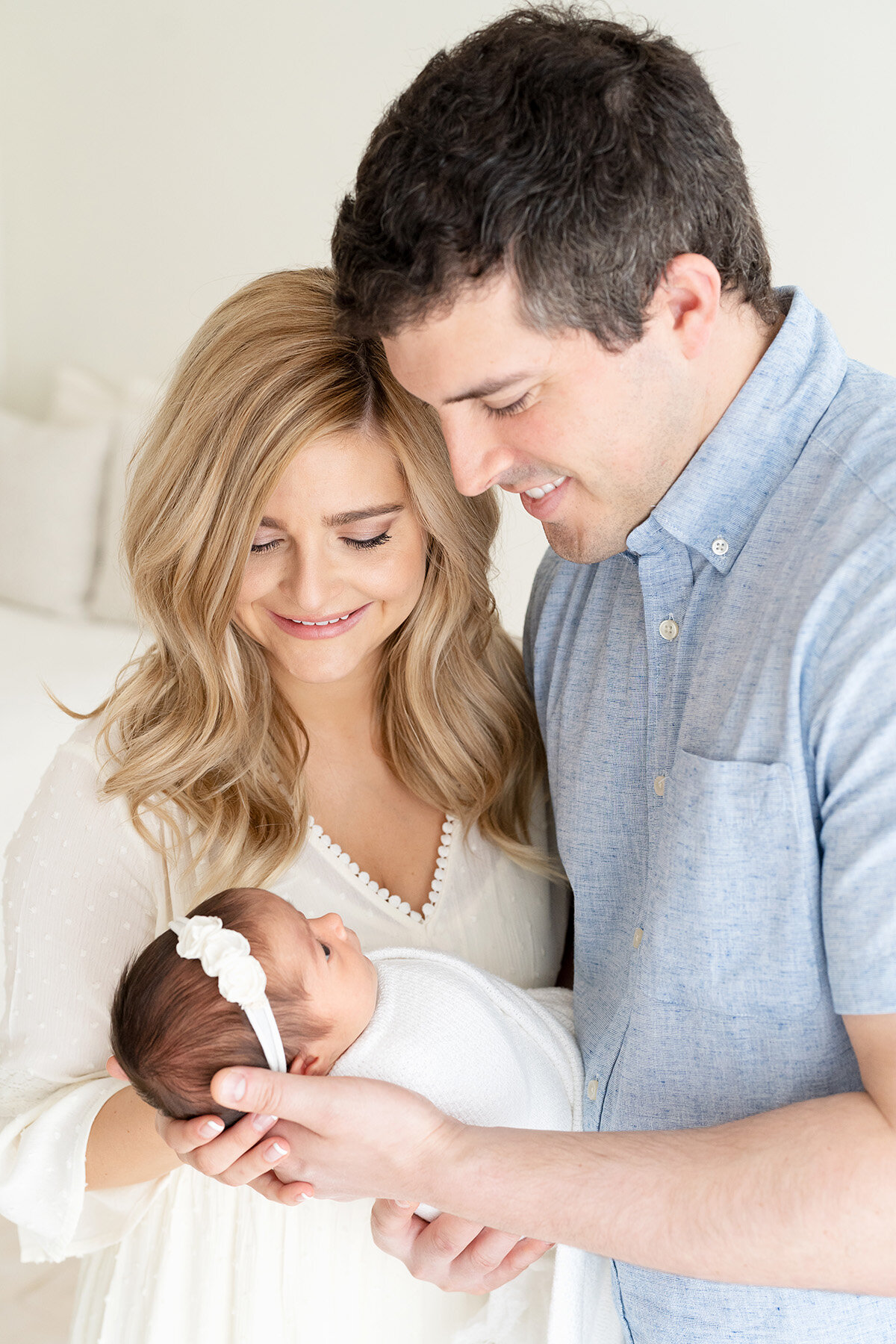 light and airy newborn photo session with mom and dad holding baby girl. baby is looking up at parents.