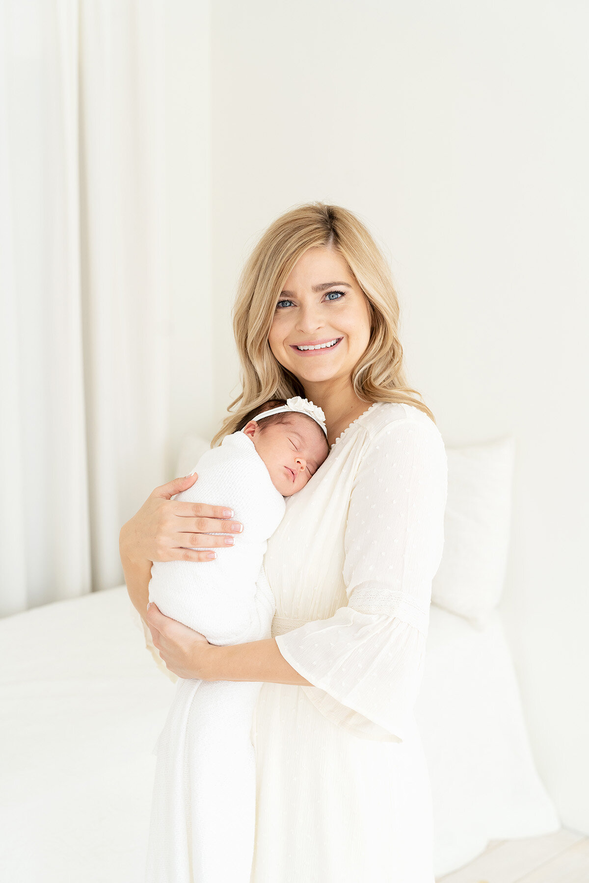 All white, light, airy, photography studio in Louisville Ky. Mom holds sleeping baby on her chest.