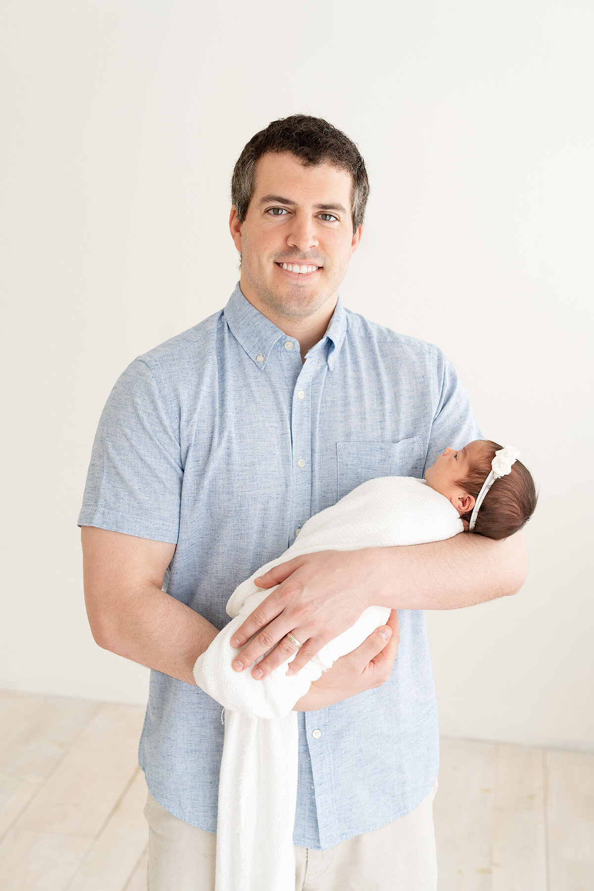 Proud dad smiles at camera while holding his newborn baby