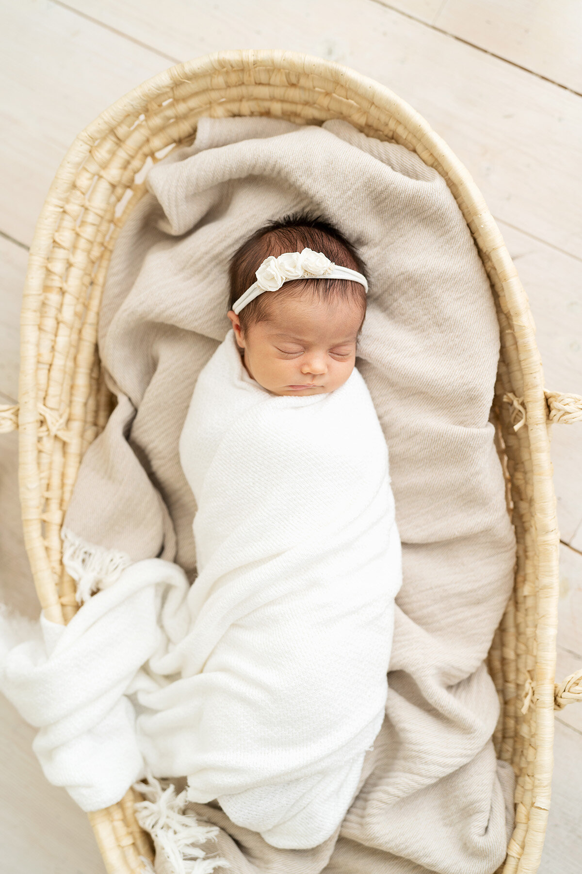 Baby sleeping in Moses basket while swaddled in white fabric