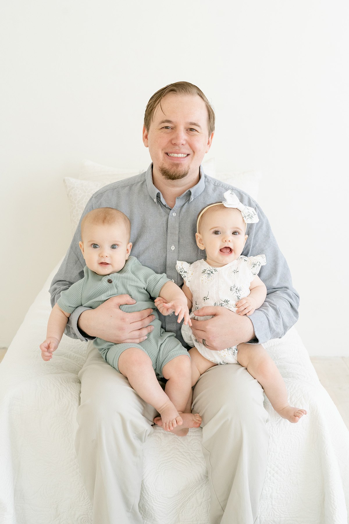Dad smiles while holding twin babies at Louisville KY photography studio with Julie Brock