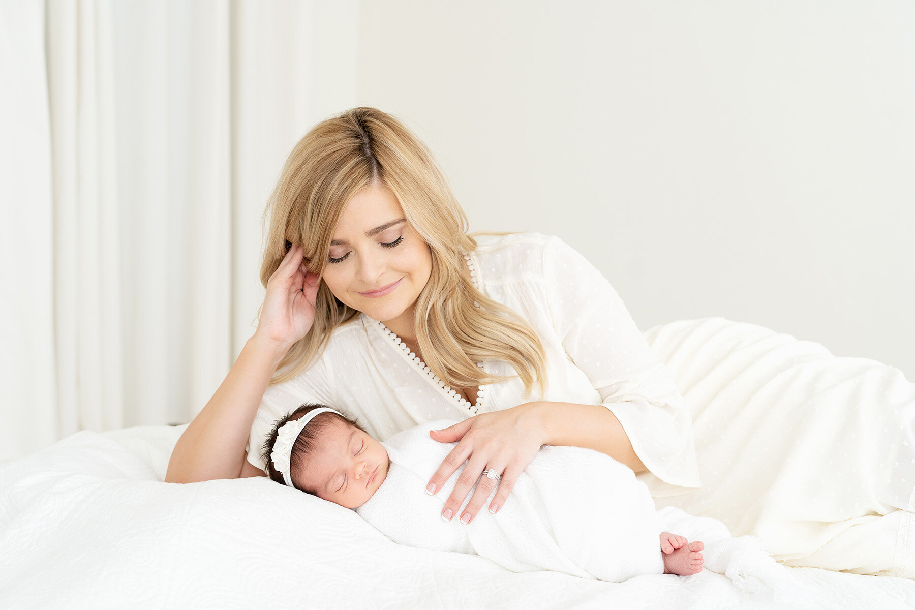 Simply styled newborn photo session with mom and baby in all white laying on bed