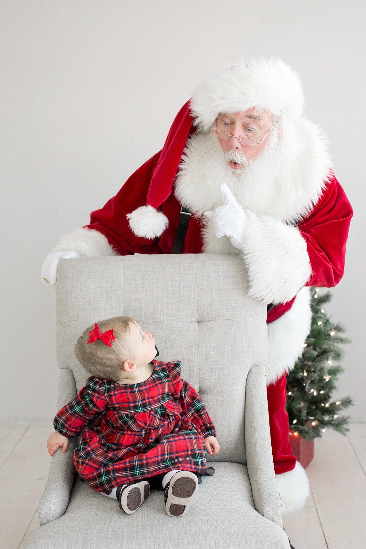Fun Santa photo of Santa sneaking up behind little girl wearing Christmas dress in Louisville Ky Julie Brock Photography
