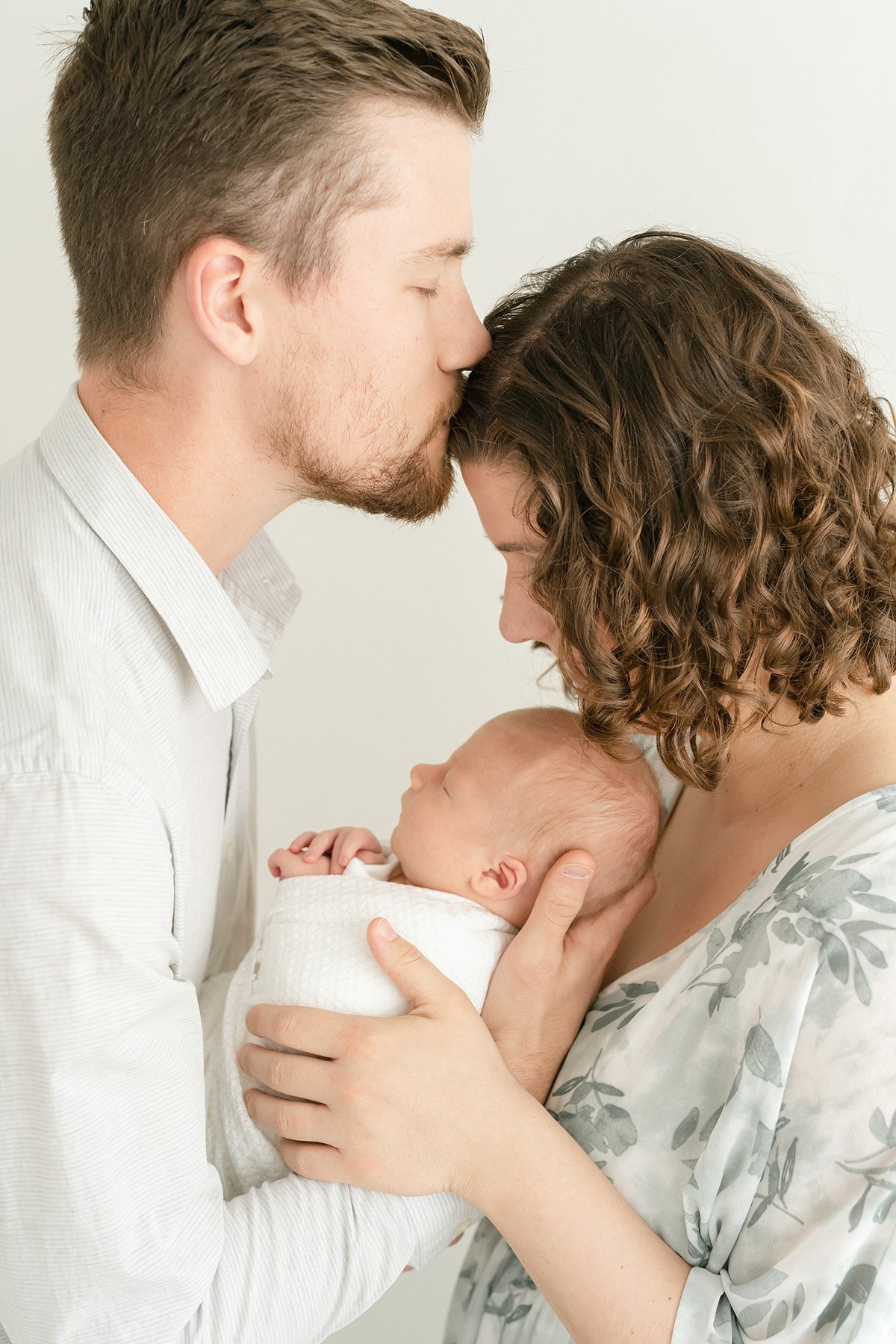 Dad kisses mom's forehead during newborn photo shoot