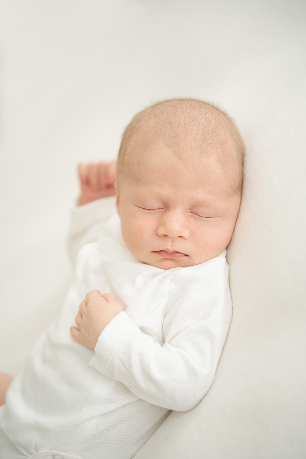 newborn baby boy in white onsie sleeps at Julie Brock Photography in Louisville KY