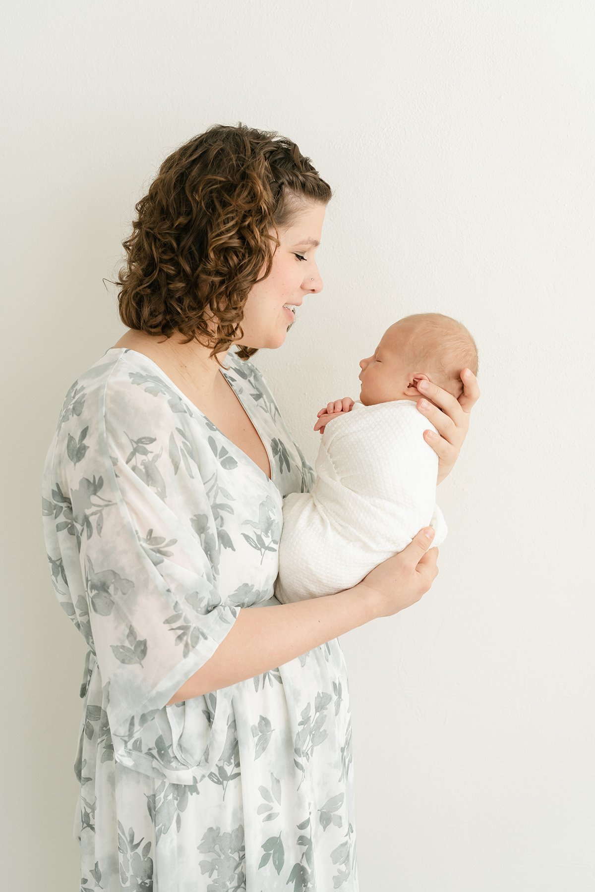 Mother wearing sage green and ivory dress holds newborn baby boy during photo shoot with Julie Brock Photography in Louisville KY