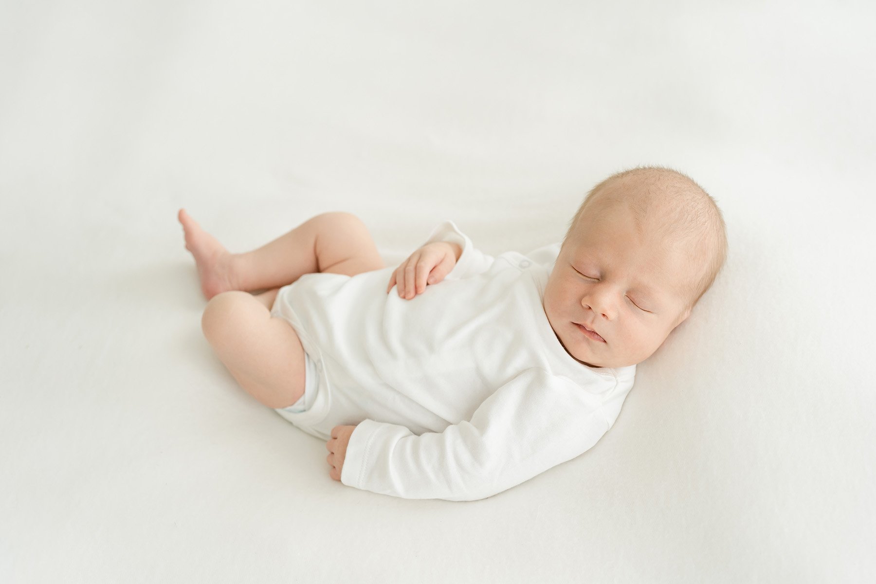 Relaxed newborn sleeping in white onsie at Julie Brock Photography in Louisville KY