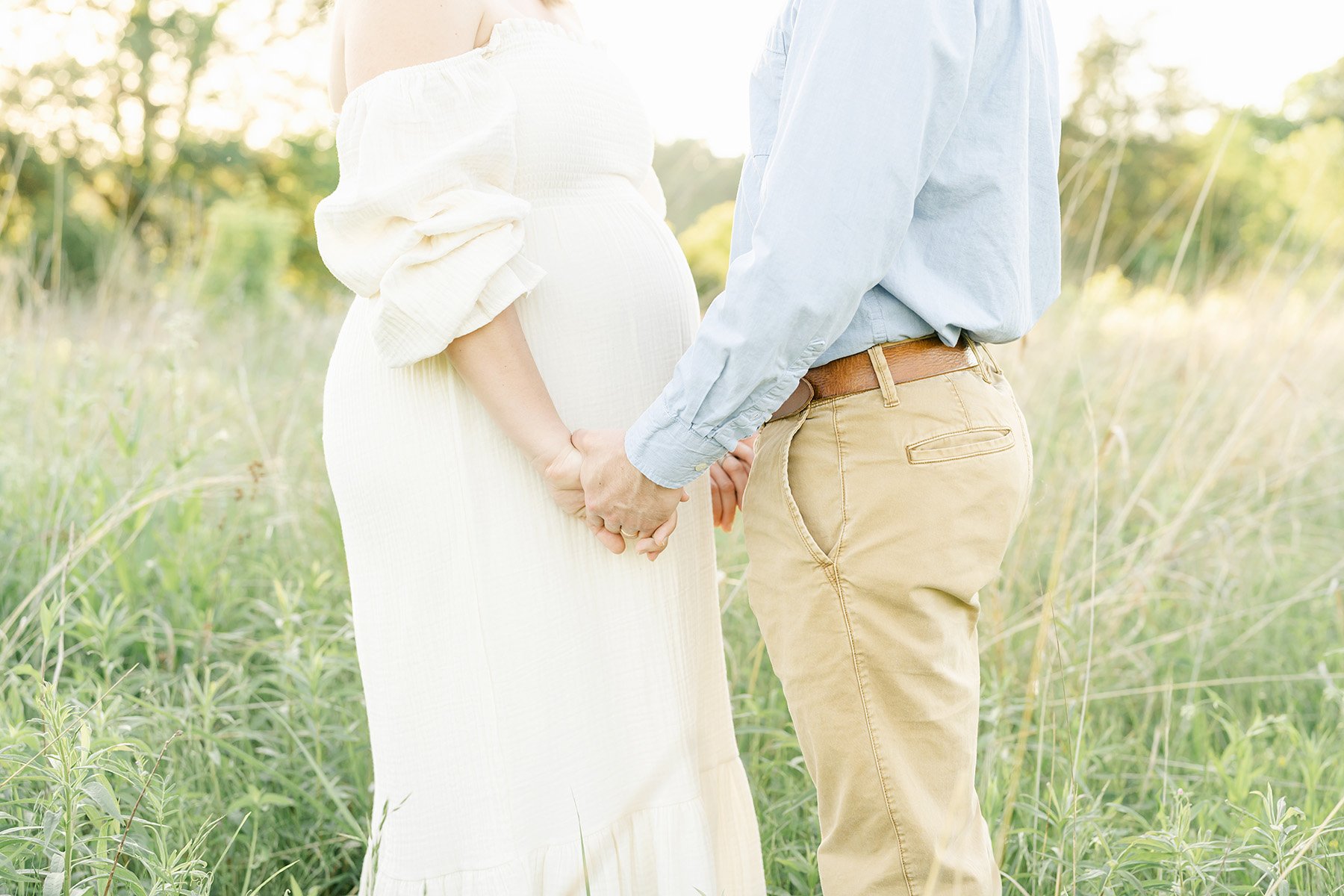 Husband and wife hold hands during sunset outdoor maternity photo shoot in Louisville KY with Julie Brock Photography