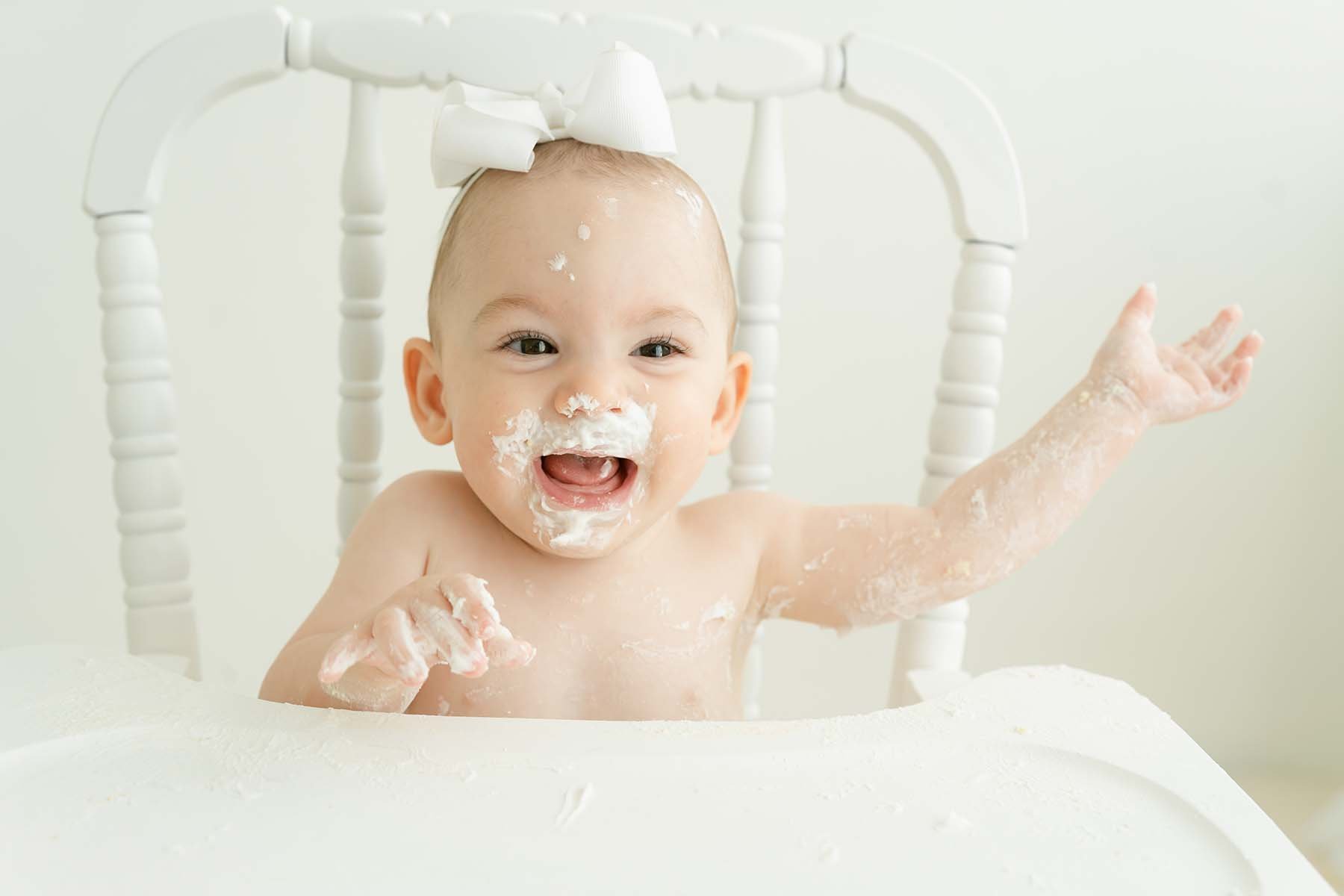 One year old baby laughs while throwing birthday cake during cake smash photo shoot at Julie Brock Photography Studio in Louisville KY