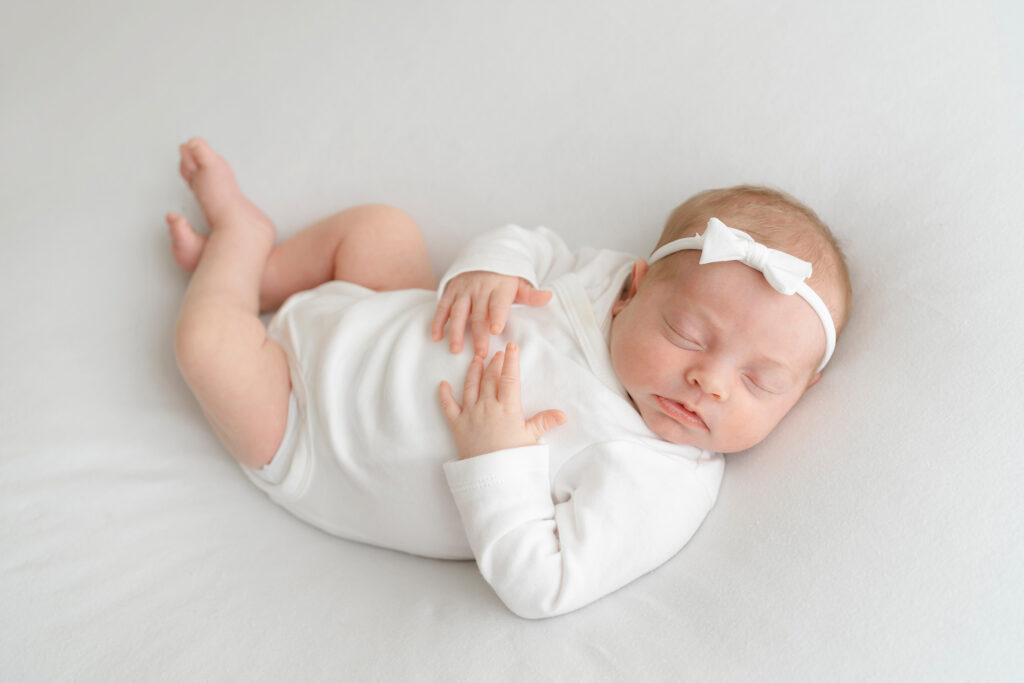 Sleepy newborn baby girl wears white bow and white onsie at Julie Brock Photography Studio in Louisville KY
