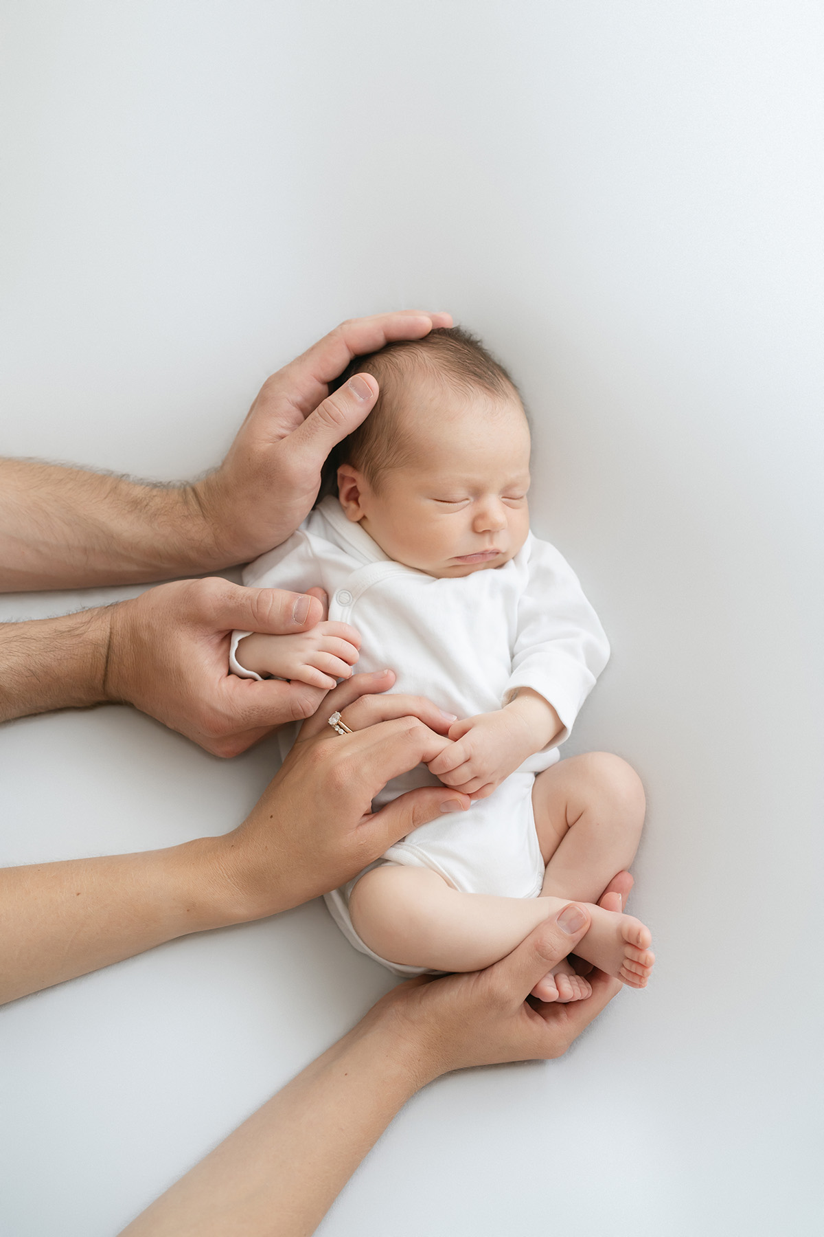 Parents wrap their hands around their sleeping newborn baby at Julie Brock Photography in Louisville KY