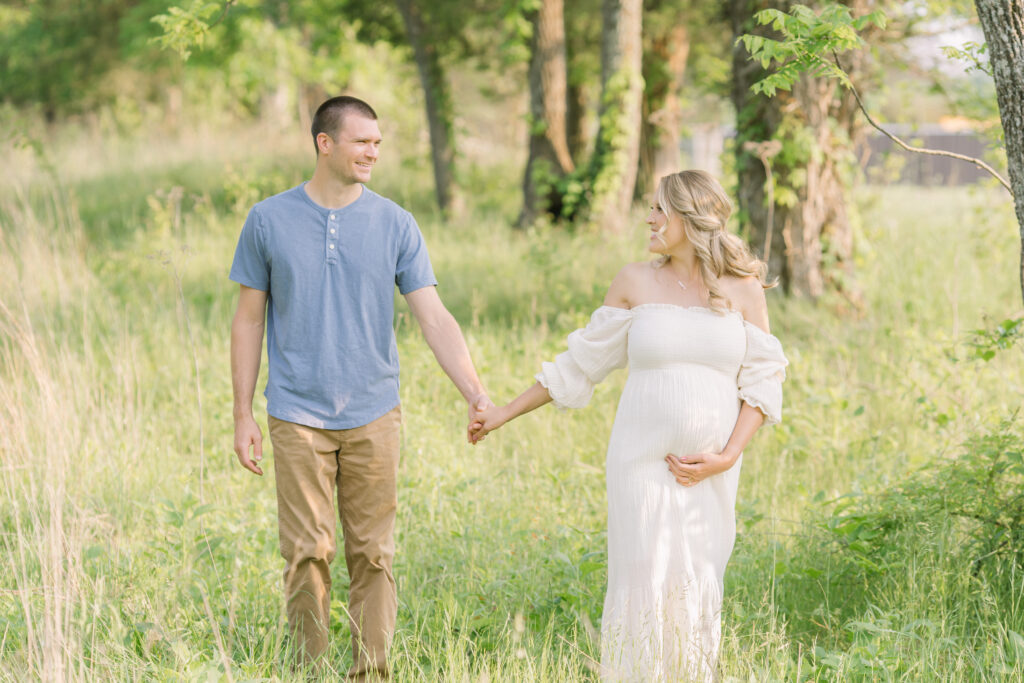 Husband and wife walk an laugh during maternity photo shoot at Louisville KY park with Julie Brock Photography