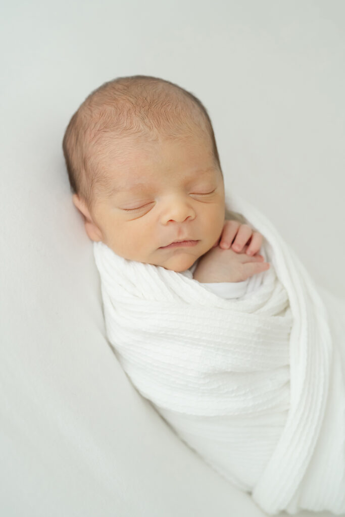 Newborn baby swaddled in a white blanket sleeps at Louisville Ky photography studio
