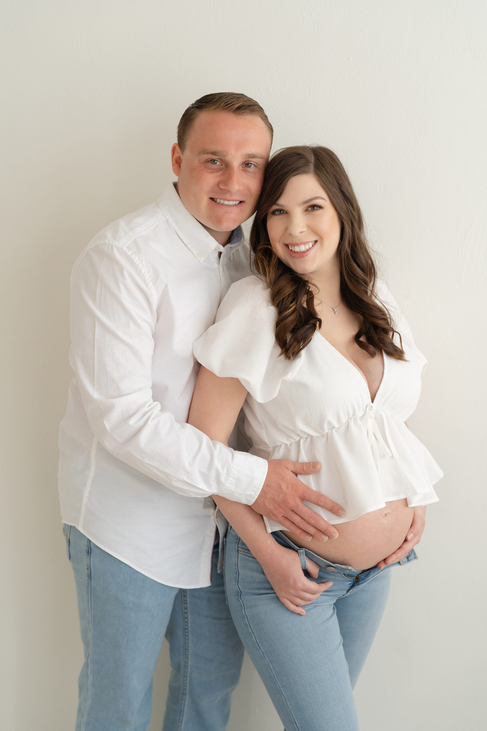 Louisville KY couple wearing modern white outfits smile during maternity pictures with photographer Julie Brock