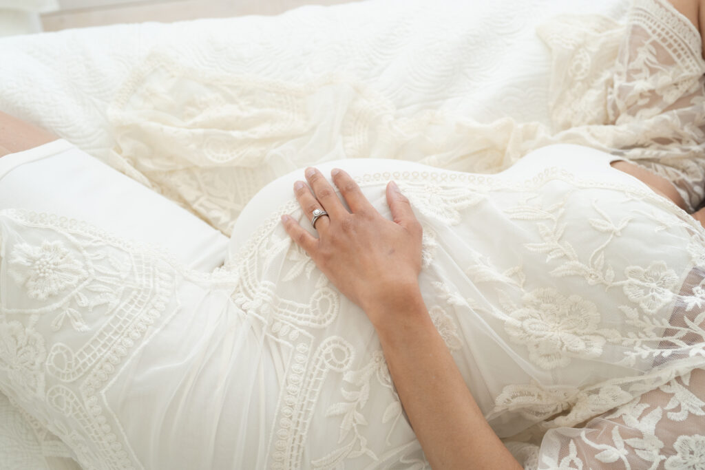 Pregnant Louisville Ky mother lays on bed for romantic profile image of her growing baby bump.