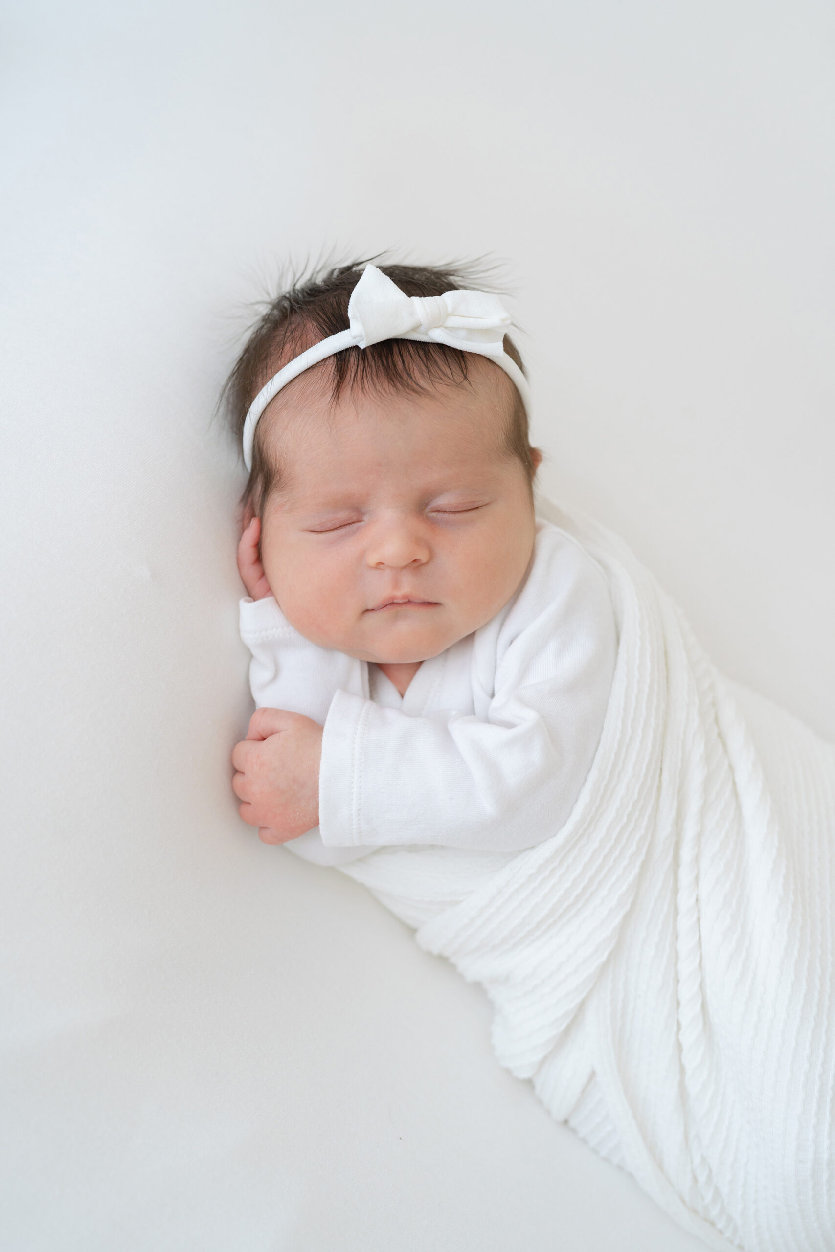 newborn baby girl is posed on her side while swaddled in a white blanket at Julie Brock Photography in Louisville KY