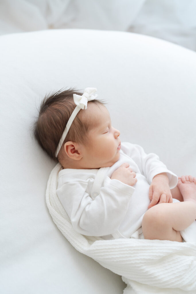 Newborn baby wearing white onsie and white headband sleeps at Julie Brock Photography in Louisville KY