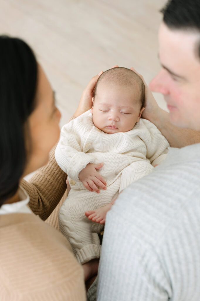 Overhead picture of parents smiling at each other while holding their sleeping baby boy who's wearing a knit sweater set for his Newborn Session with Julie Brock Photography in Louisville KY