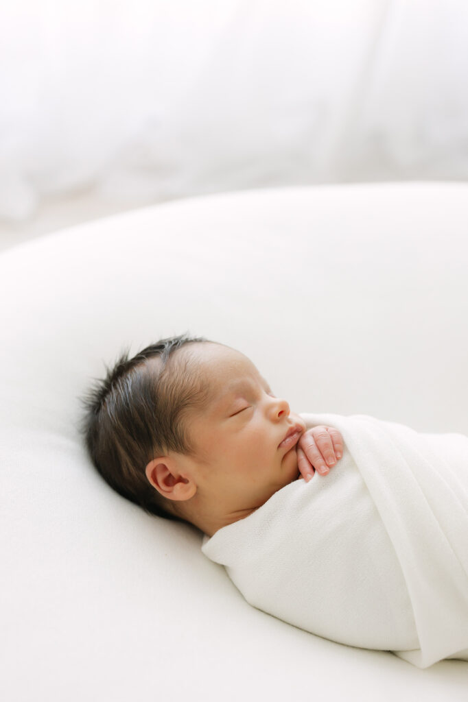 Newborn baby boy is swaddled in soft white wraps and being photographed by Louisville Newborn Photographer Julie Brock