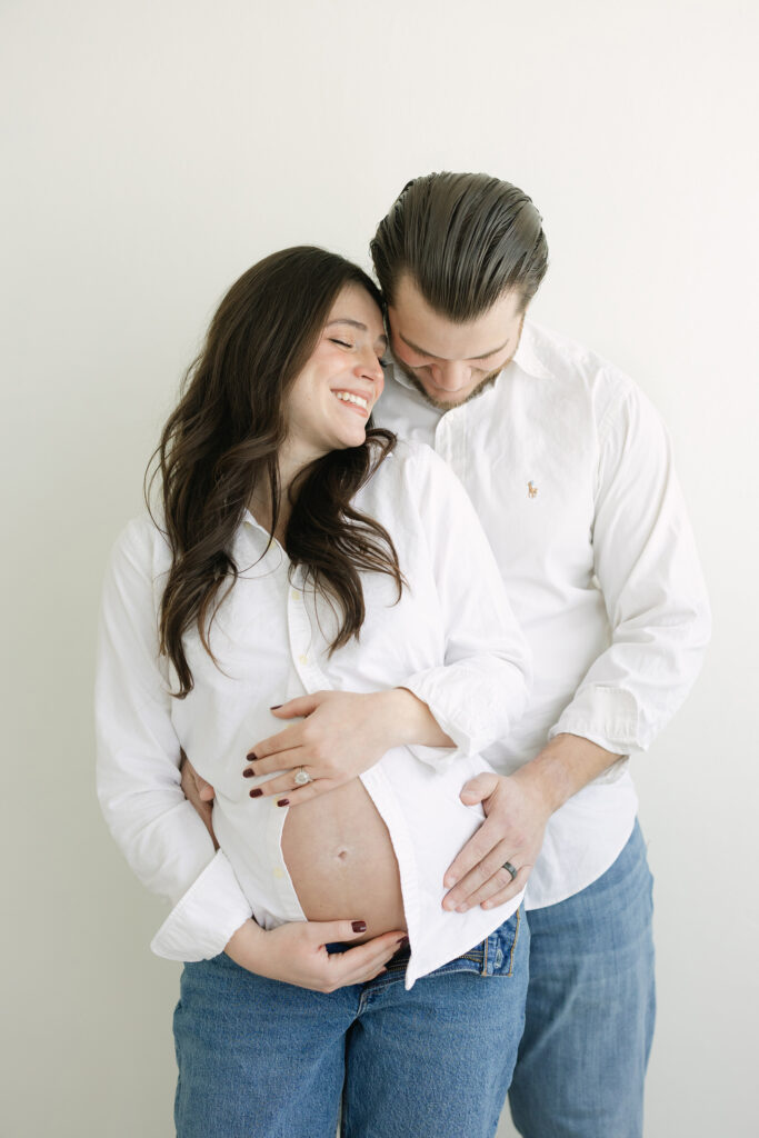 Dad hugs his pregnant wife, both wearing relaxed jeans for Maternity Photo Session in studio near Louisville KY with photographer Julie Brock