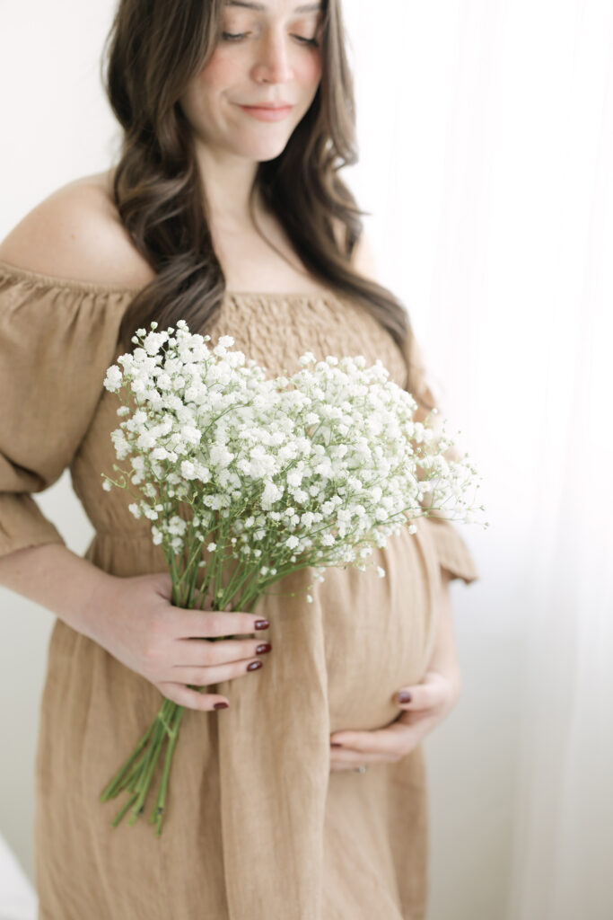 Pregnant mother holds flowers near her round belly at her Maternity Session at Julie Brock Photography studio near Louisville KY
