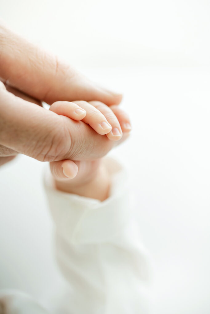 Proud Mom holds their sleeping infant's hand during a Newborn Session in our natural light studio near the St Matthews KY area of Louisville, KY by Julie Brock Photography.