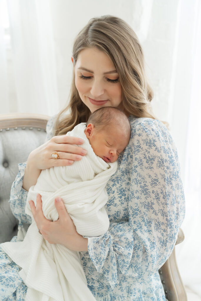 Mom wearing blue dress and ivory dress for newborn photo shoot while holding her baby during a newborn photo session in Louisville, KY studio