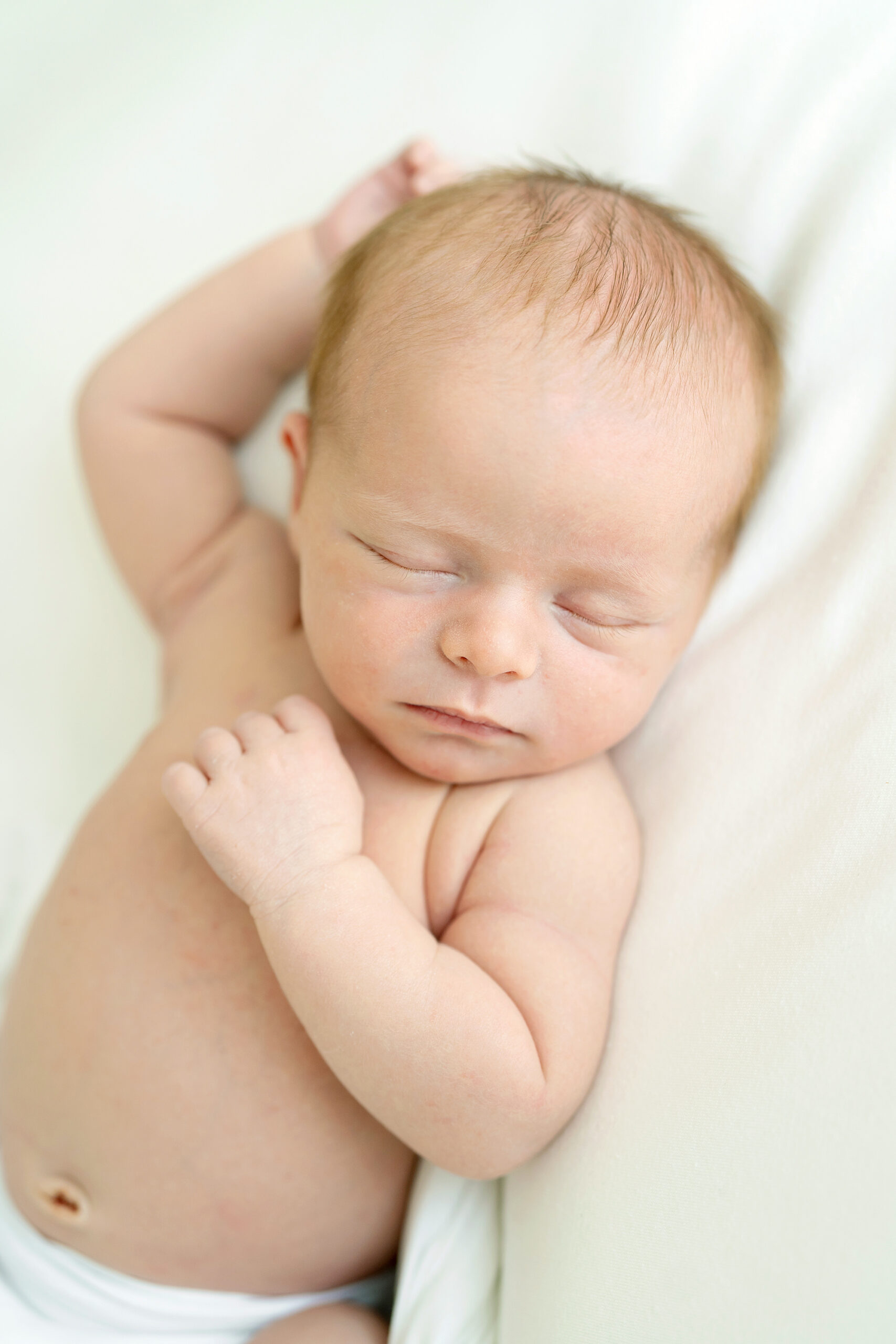 Infant boy sleeps with one hand stretched out cheek and the other hand on his chest during a Newborn Session by Julie Brock Photography near the St Matthews area of Louisville KY.