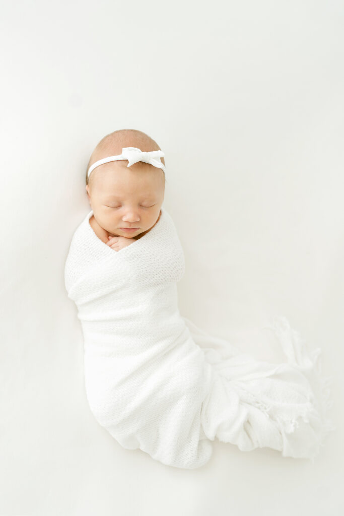 the best time to book newborn photos to have dreamy images like this newborn baby sleeping on a white blanket during her Newborn Photo Session near Louisville KY at Julie Brock Photography