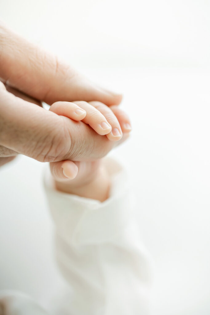 Up close detail image of dad holding his newborn baby's tiny hand during their Newborn Photography Session near Louisville KY at Julie Brock Photography's newborn photo studio