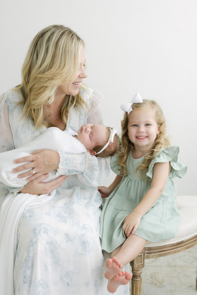 Big sister smiles and laughs for a photo with her infant sister at newborn photography studio near louisville ky