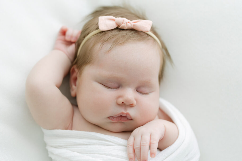 Infant girl sleeps with her arms stretched above her head during newborn photo shoot with Louisville Photographer Julie Brock