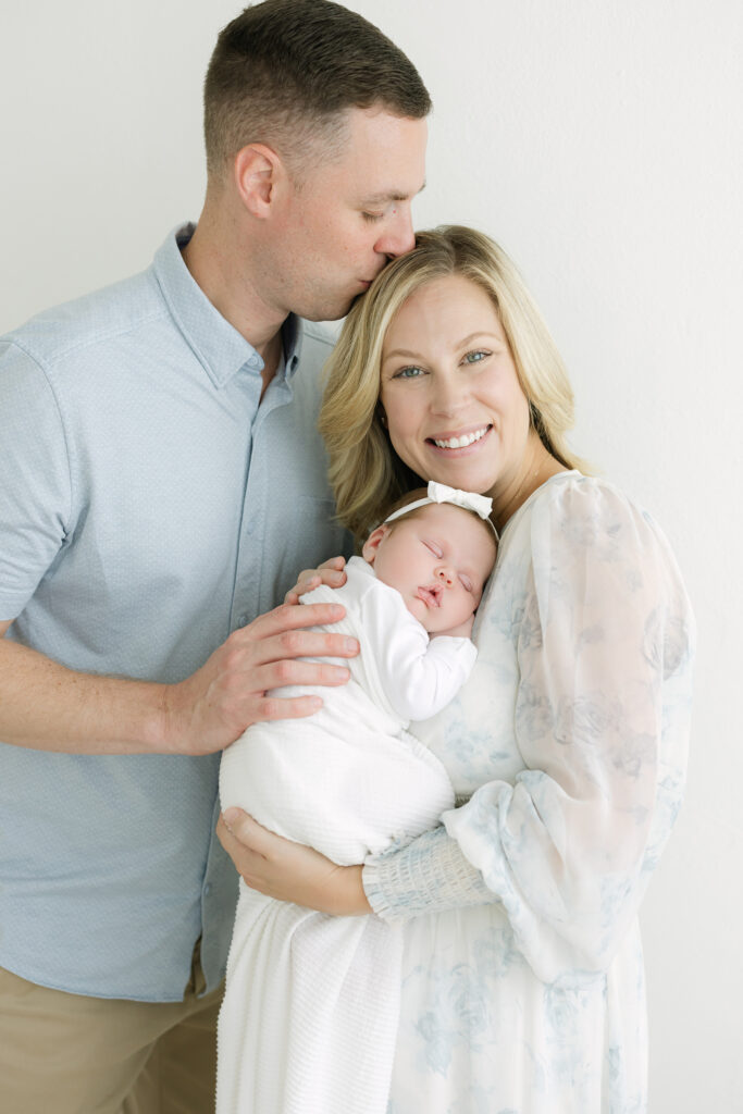 Dad kisses his wife's forehead during their newborn photo session with Louisville Newborn Photographer Julie Brock